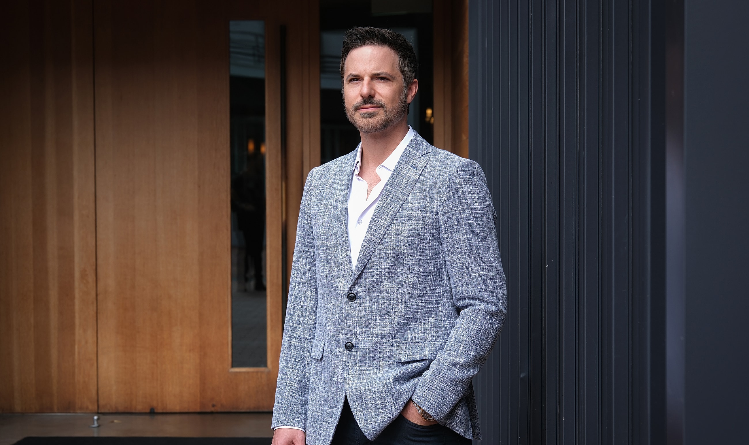 Man in stylish blazer standing by entrance.